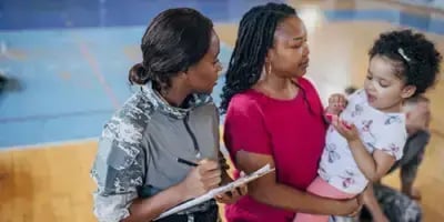 Mother holding daughter as a child welfare agencies takes notes.